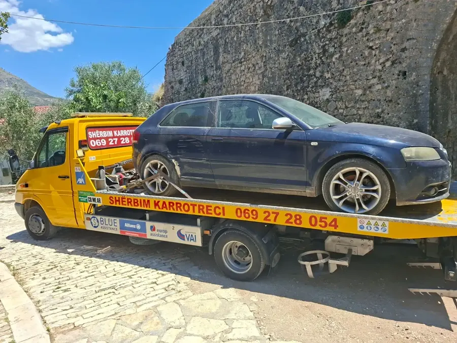 Yellow tow truck loading a damaged car near Gjirokastër castle