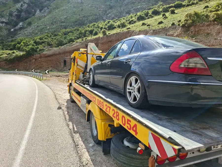 Flatbed tow truck carrying a dark sedan on a mountain road