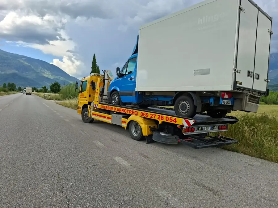 Flatbed tow truck finishing loading a blue cargo van