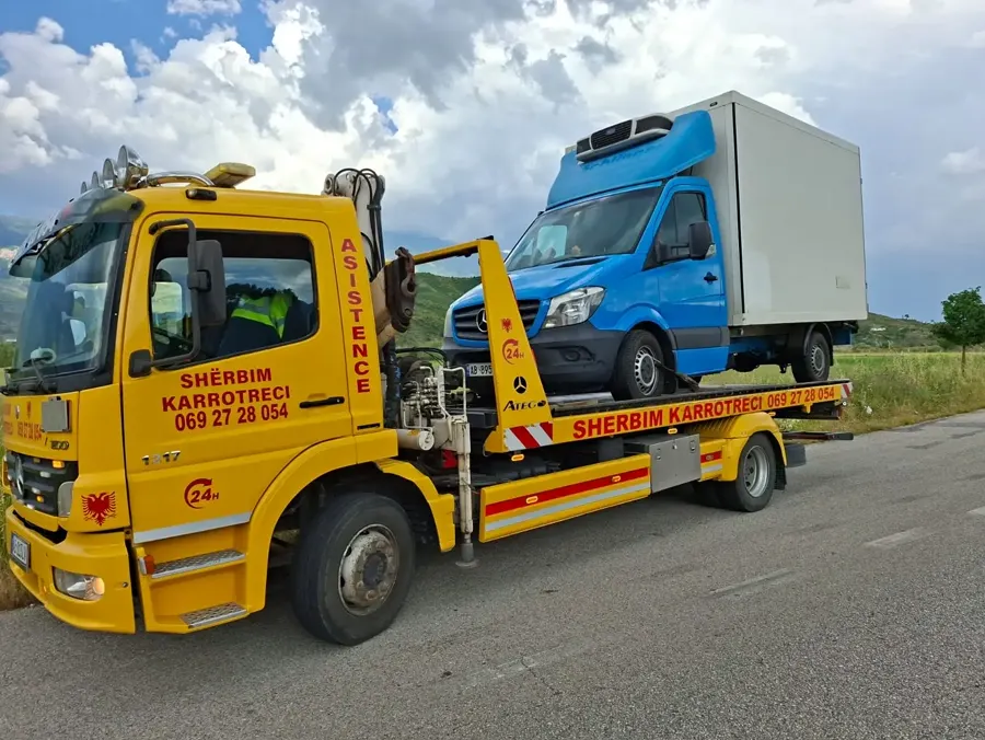 Flatbed tow truck loading a blue cargo van on a mountain road