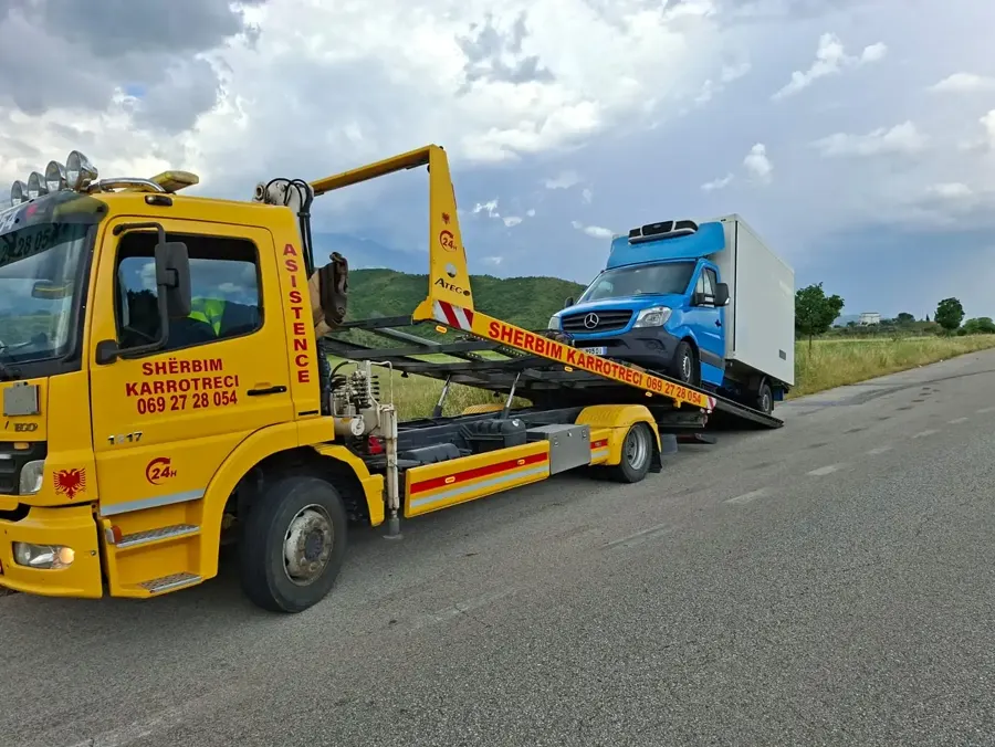 Flatbed tow truck with a blue cargo van loaded, mountain road