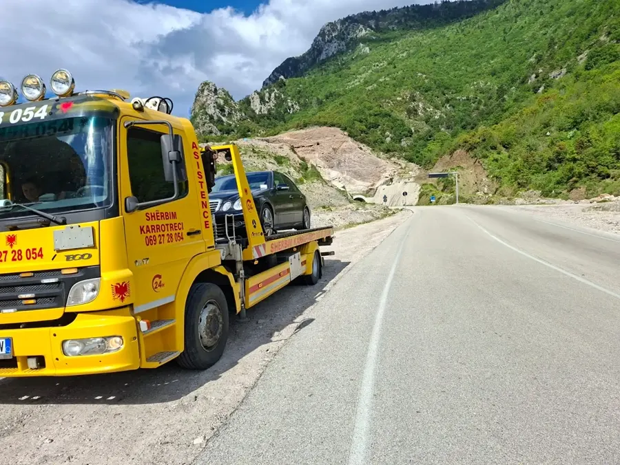 Flatbed tow truck carrying a sedan on a mountain highway near a tunnel