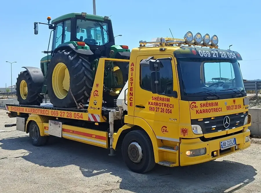 Flatbed tow truck loading a tractor with its crane