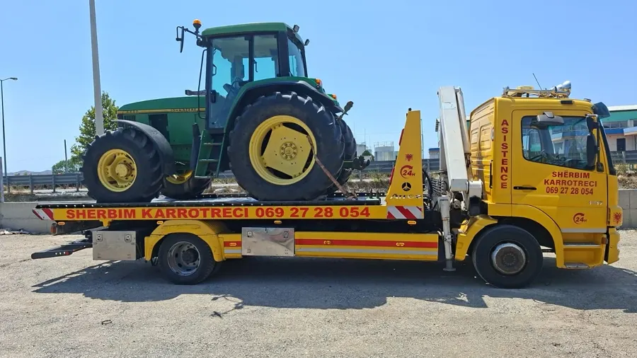 Flatbed tow truck with a green tractor loaded, crane extended