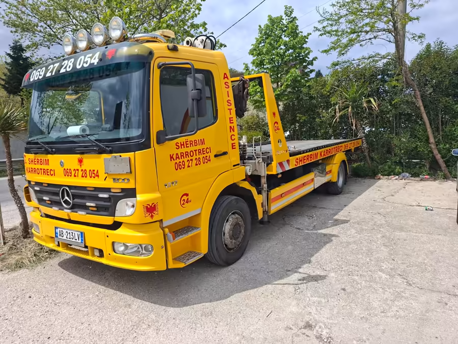 Flatbed tow truck using its crane to load a tractor in a rural mountain area
