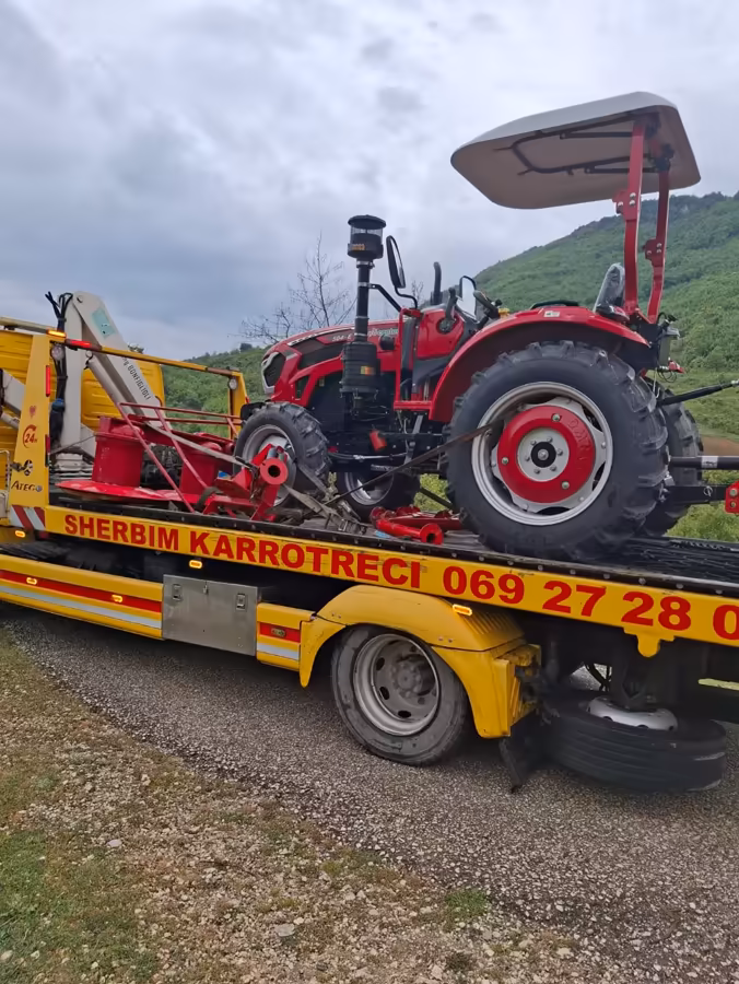 Yellow tow truck transporting a tractor through a rural mountain area