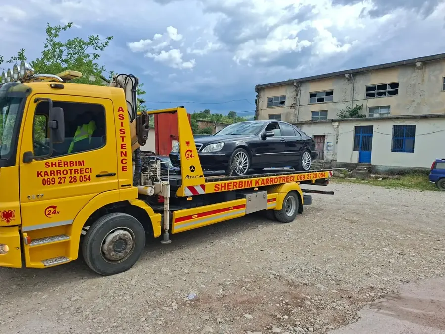 Flatbed tow truck with a black sedan loaded, parked in a yard