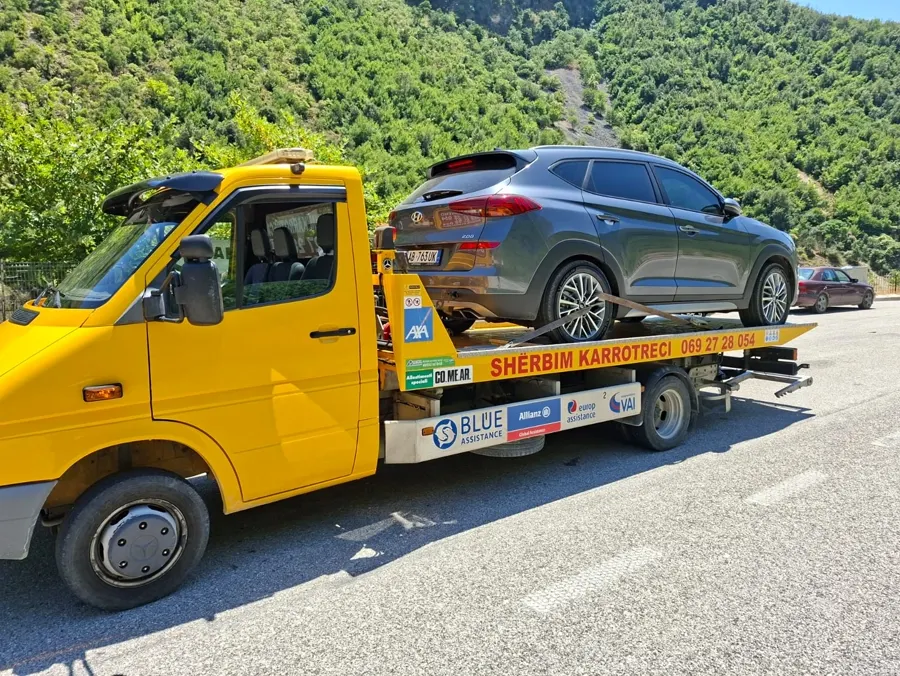 Flatbed tow truck carrying a gray SUV on a mountain road