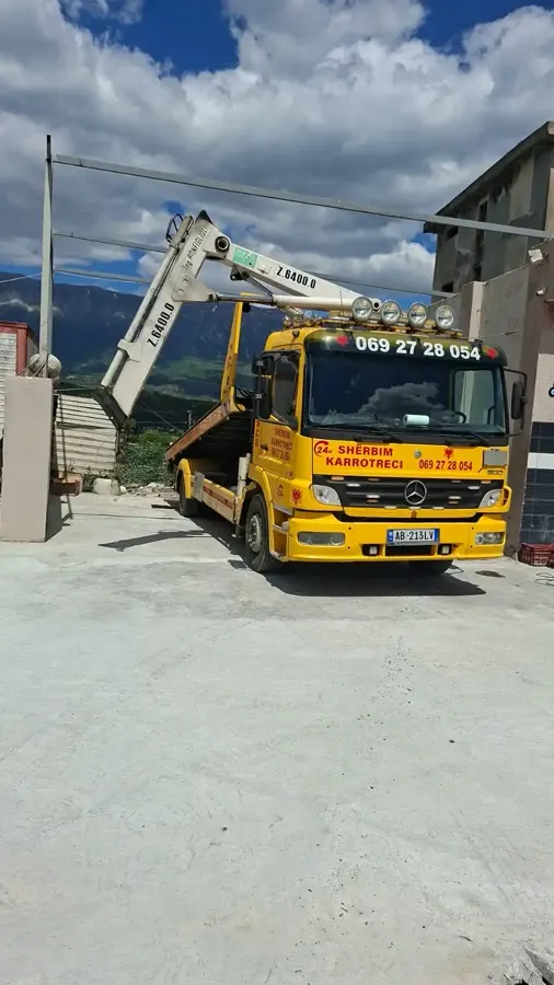 Yellow tow truck with crane parked at base, mountains in the background