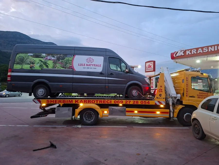 Tow truck loading a delivery van at dusk near a fuel station