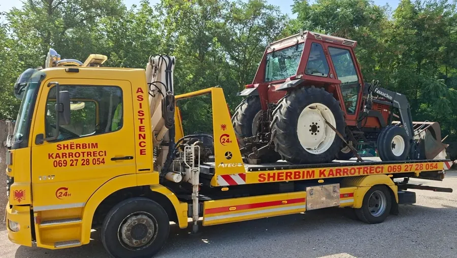 Flatbed tow truck loading a vintage tractor in a rural yard